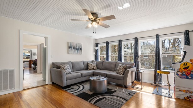 A modern living room with a sectional sofa, a coffee table, and a ceiling fan. - Game Themed, sleeps 12, king beds, walking distance to downtown & splash pad! (Harrison)