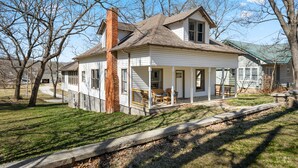 A two-story house with a porch, a chimney, and a small front yard. - Game Themed, sleeps 12, king beds, walking distance to downtown & splash pad! (Harrison)