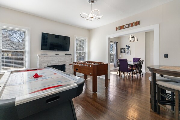 A living room with a foosball table, a fireplace, a television, and a dining area with chairs and a table.