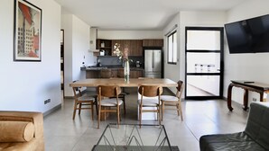 Een moderne keuken met houten kasten, een roestvrijstalen koelkast, en een eethoek met een glazen tafel en houten stoelen.