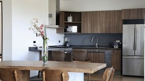 Een moderne keuken met houten kastjes, een roestvrijstalen koelkast en een eethoek met een houten tafel en stoelen.