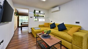 A modern living room with a yellow sofa, a coffee table with a bowl of fruit, and a flat-screen TV mounted on the wall. - Cozy home in Legrad with sauna (Legrad)