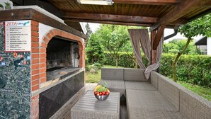 An outdoor patio with a brick oven, wicker furniture, and a bowl of fruit. - Cozy home in Legrad with sauna (Legrad)