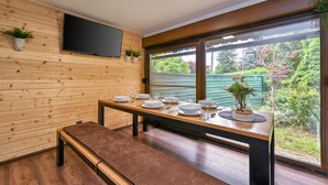 A modern room with wooden panel walls, a flat-screen TV mounted above a dining table set for four, and a bench. - Cozy home in Legrad with sauna (Legrad)