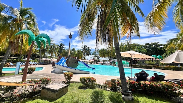 A pool area with a boat-shaped slide, palm trees, and lounge chairs.