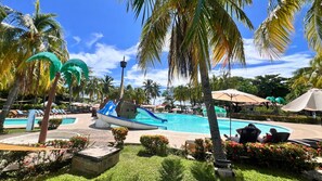 Un área de piscina con un tobogán con forma de barco, palmeras y sillas de descanso.