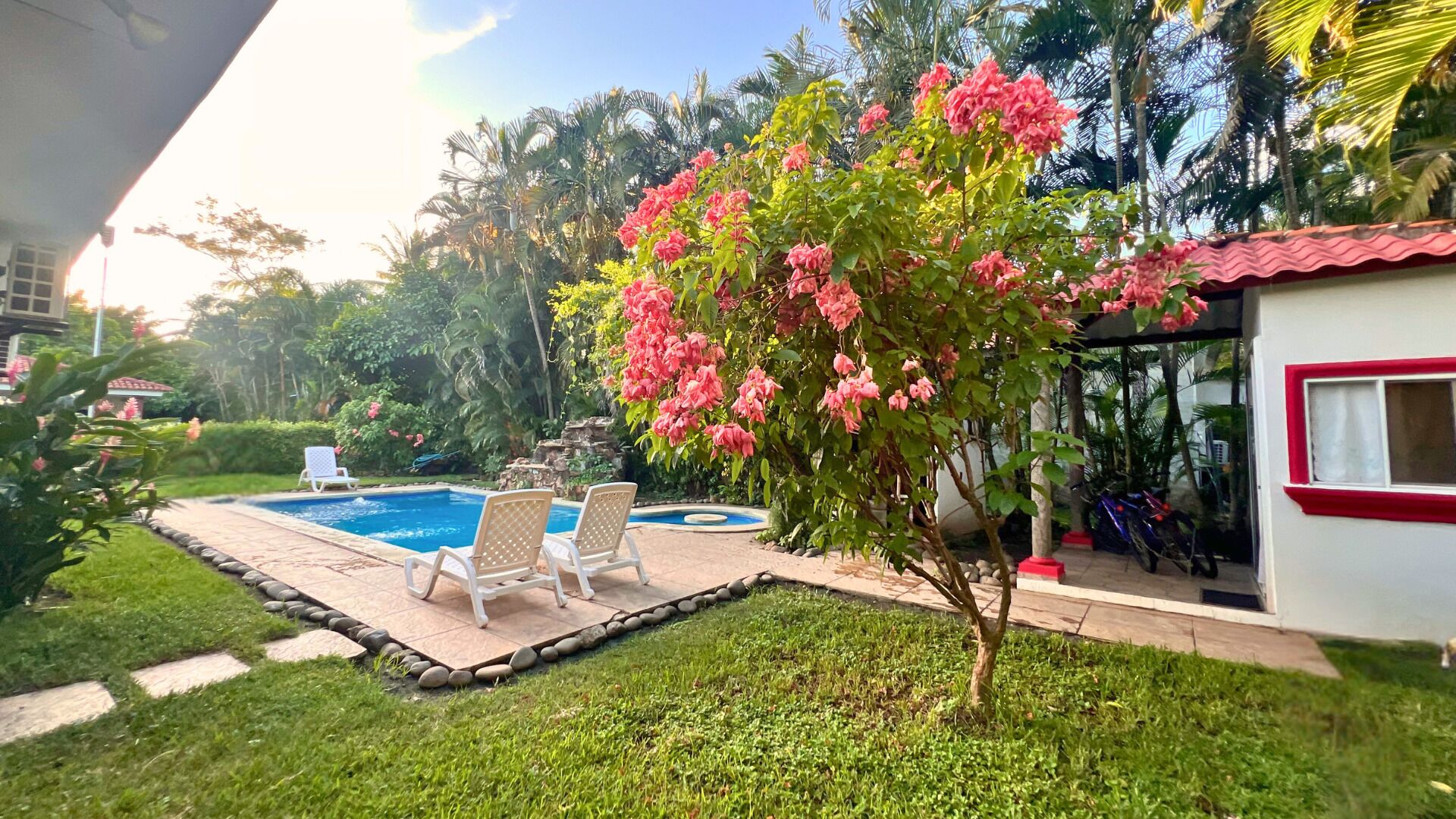 A swimming pool with lounge chairs, a small garden, and a building with a red trim.