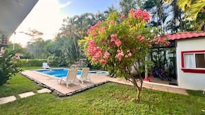 A swimming pool with lounge chairs, a small garden, and a building with a red trim. - Quinta Luna Mar (Acajutla)