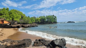 A beach with rocky shoreline, clear blue water, and lush greenery.