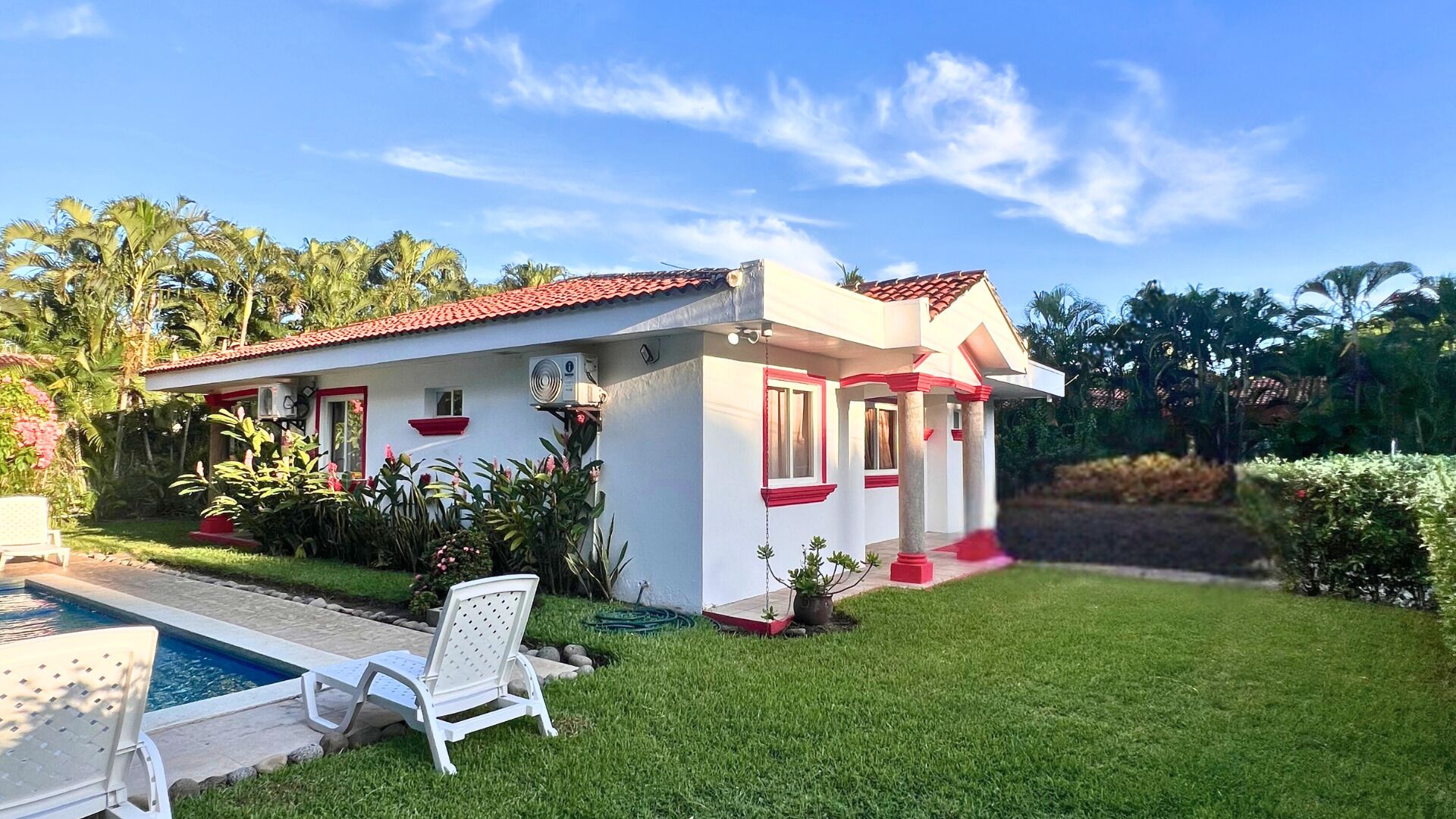 A house with a swimming pool, a covered patio, and lush greenery.