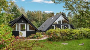 Zwei moderne Blockhütten mit Satteldächern, umgeben von üppigem Grün und Bäumen.