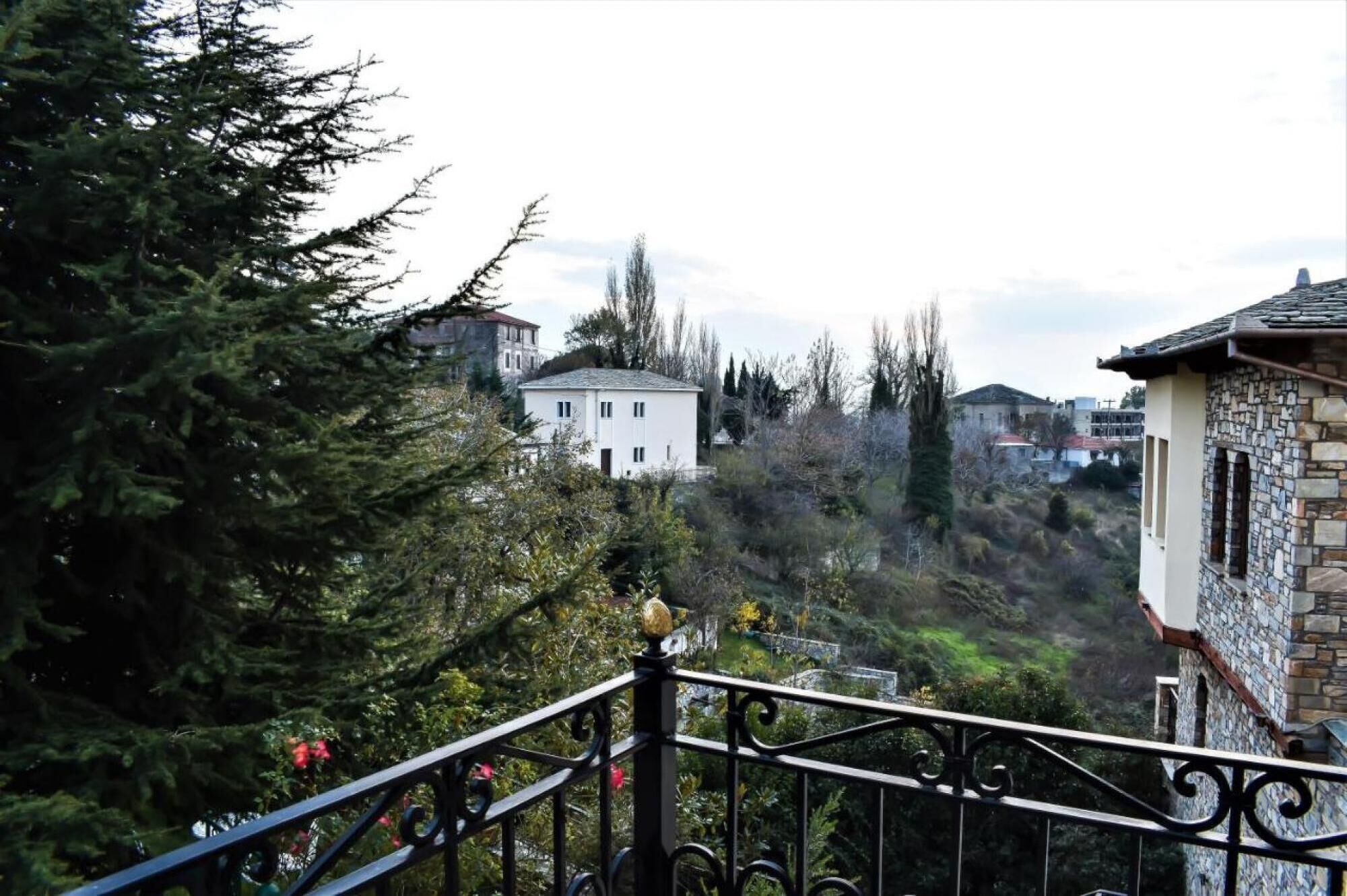 A residential area with a white house, a stone building, and dense greenery.