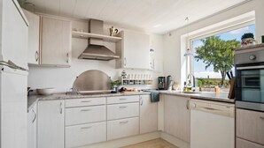 A modern kitchen with white cabinetry, a stainless steel range hood, a built-in oven, and a window offering a view of the outdoors. - Awesome home in Slagelse with WiFi (Slagelse)