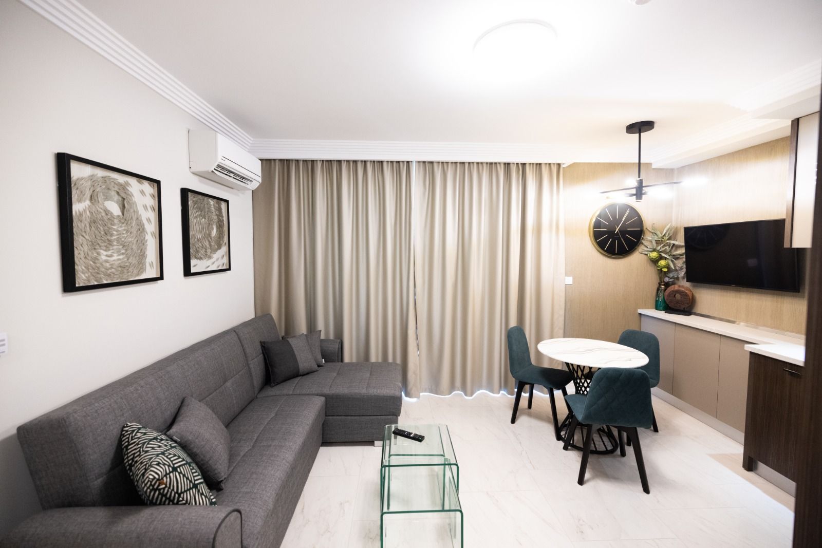 A modern living room with a grey sectional sofa, a glass coffee table, and a dining area with a round table and chairs.