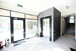 A modern building entrance with glass doors, a fire extinguisher, and an exit sign. - Ava Apart By Nora (Timisoara)