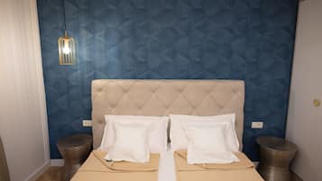 Ein Schlafzimmer mit einer gesteppten Kopfstütze, zwei weißen Kissen, einer beigen Bettdecke, zwei Nachttischen und einer hängenden Leuchte.