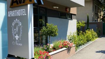 An apartment hotel with a sign reading 'APARTHOTEL Nora' and a small garden with various plants and flowers.