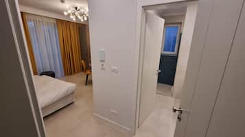 A hotel room with a bed, a chair, a desk, a window with curtains, and a door leading to a bathroom.