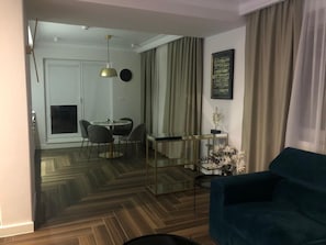 Un salon moderne avec un canapé, un coin repas avec des chaises, une table en verre et une œuvre d’art accrochée au mur.