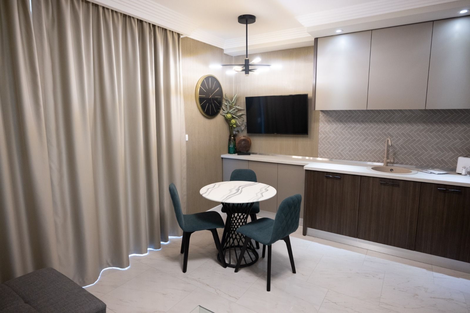 A modern kitchen with a dining area, featuring a round table, chairs, a TV, and a built-in oven.