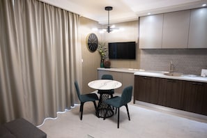 A modern kitchen with a dining area, featuring a round table, chairs, a TV, and a built-in oven. - Ava Apart By Nora (Timisoara)