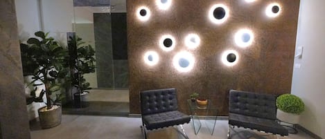A reception area with two upholstered chairs, a wall-mounted light fixture, and a potted plant.