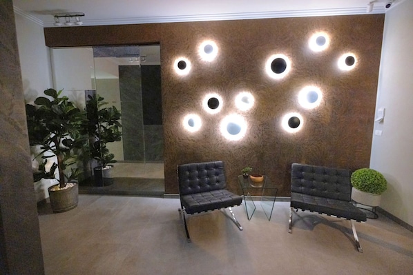 A reception area with two upholstered chairs, a wall-mounted light fixture, and a potted plant. - Ava Apart By Nora (Timisoara)