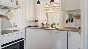 Een keuken met witte kasten, een fornuis, een spoelbak en hangende messen.