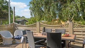Een terras buiten met rieten stoelen en een tafel, omgeven door een houten hek en bomen.