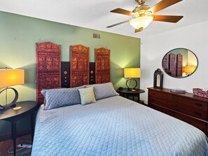 Une chambre à coucher comprenant un lit, deux tables de chevet, une commode, un ventilateur de plafond et un miroir fixé au mur.