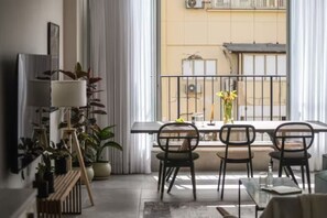 Un salon moderne avec balcon, comprenant une table à manger avec des chaises, un lampadaire et des plantes en pot.