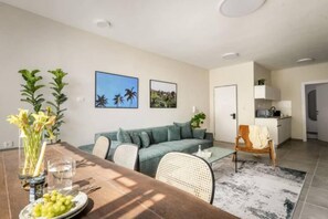A modern living room with a sofa, a dining table with a vase of flowers, and a kitchen area in the background. - Spacious & Bright 3BR Apartment (Tel Aviv-Jaffa)