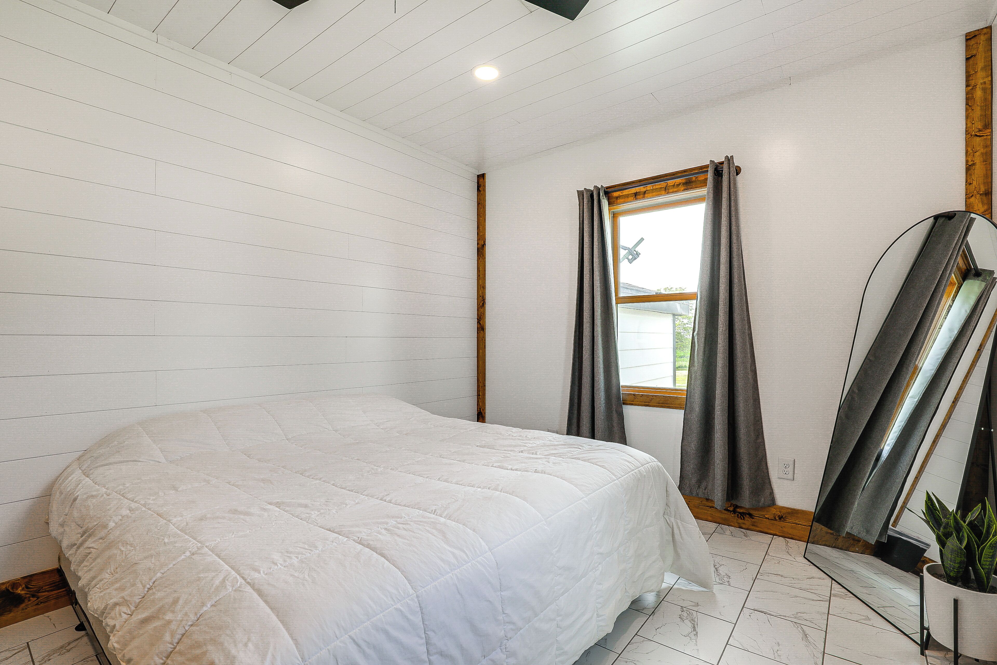 Quarto com cama grande, janela com cortinas e espelho na parede.