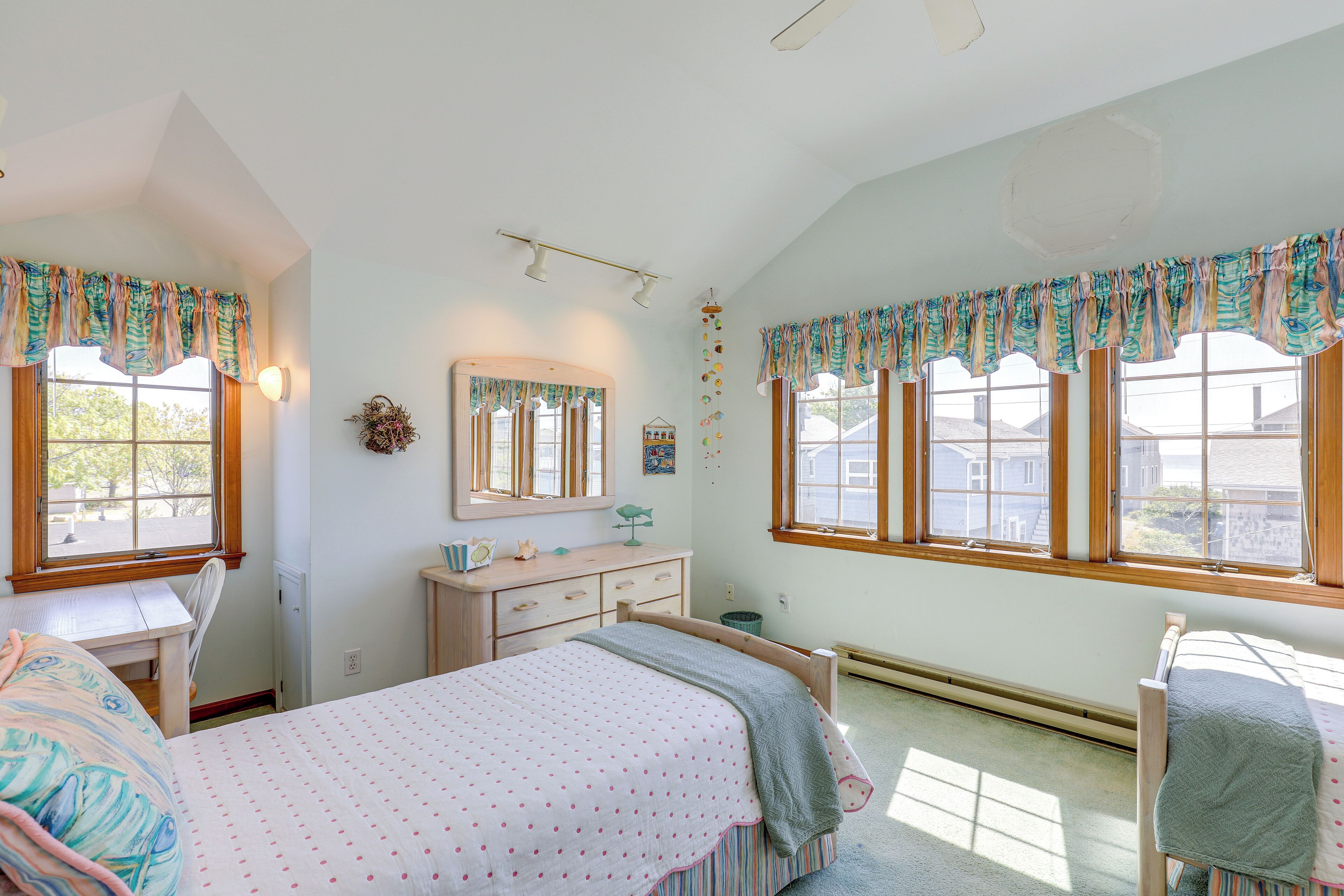 A bedroom with a bed, a desk, a dresser, and a window with curtains.