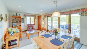 Un salon chaleureux avec un coin repas, des meubles en bois et une vue sur l’extérieur.