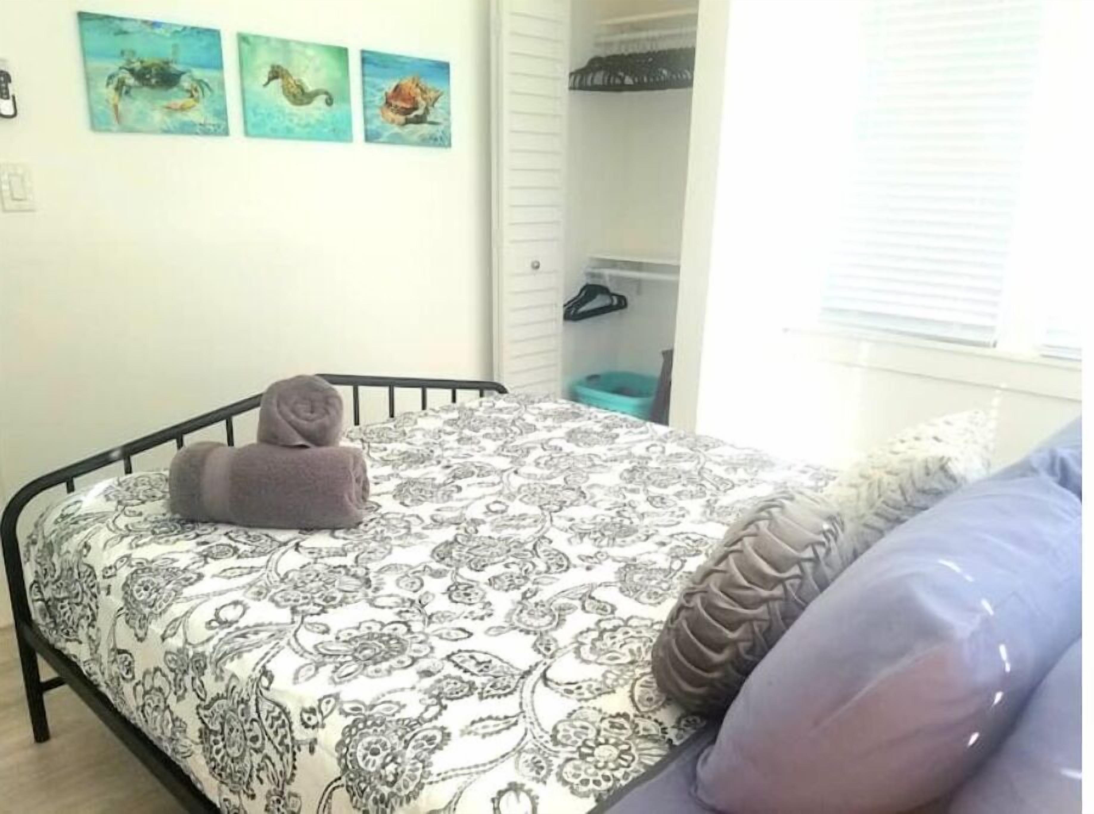 A bedroom with a bed, a pillow, a rolled towel, and three wall art pieces.