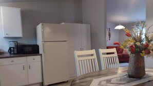 Une cuisine compacte équipée d’un réfrigérateur, d’un four à micro-ondes et d’une machine à café. On y trouve une table à manger avec deux chaises et un vase de fleurs.