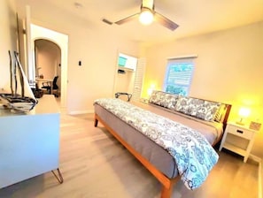 Une chambre à coucher avec un lit, des tables de chevet, un bureau et un ventilateur de plafond.