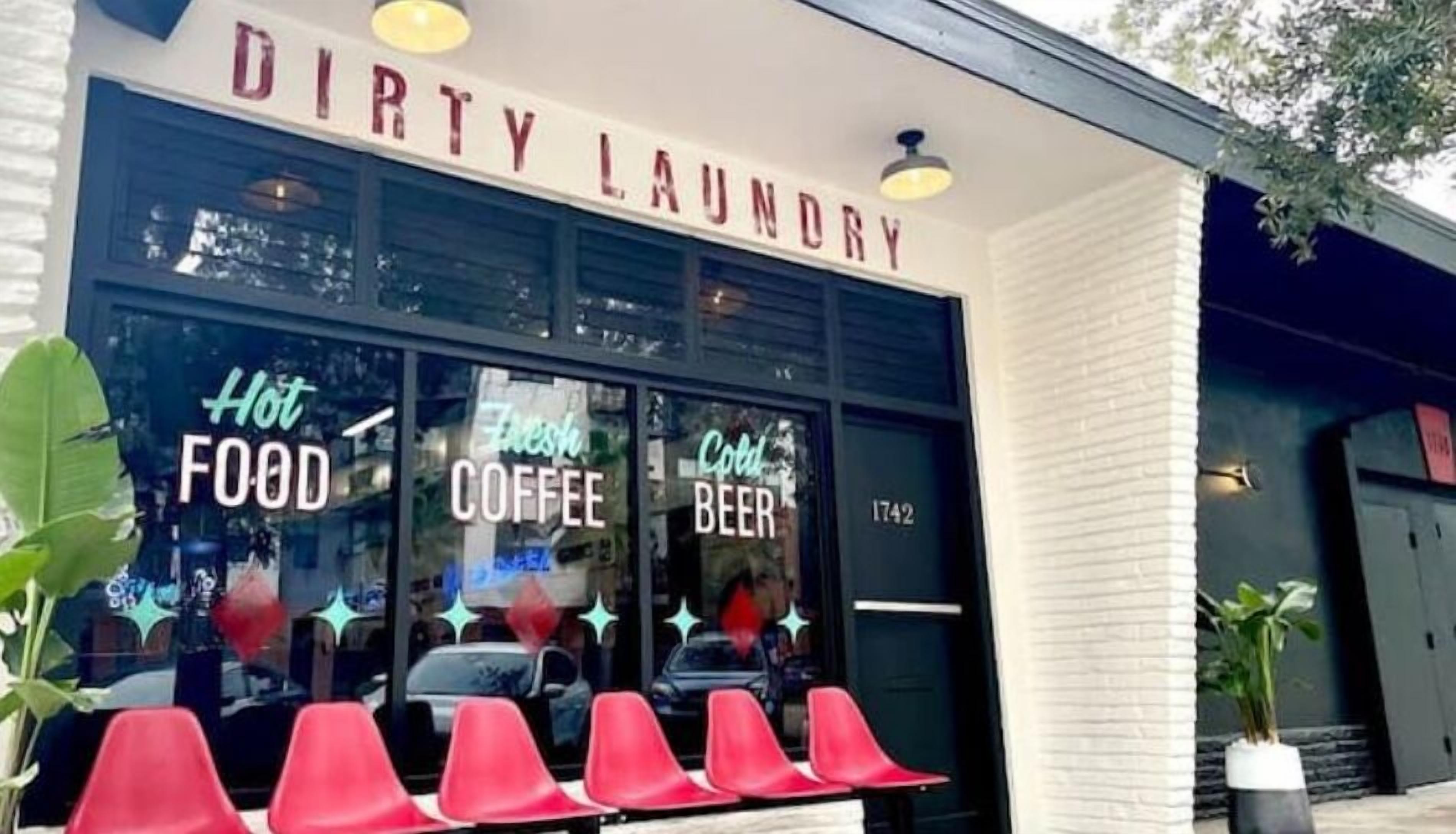 A storefront with a sign reading "DIRTY LAUNDRY" and neon signs advertising "Hot FOOD," "Fresh COFFEE," and "Cold BEER."