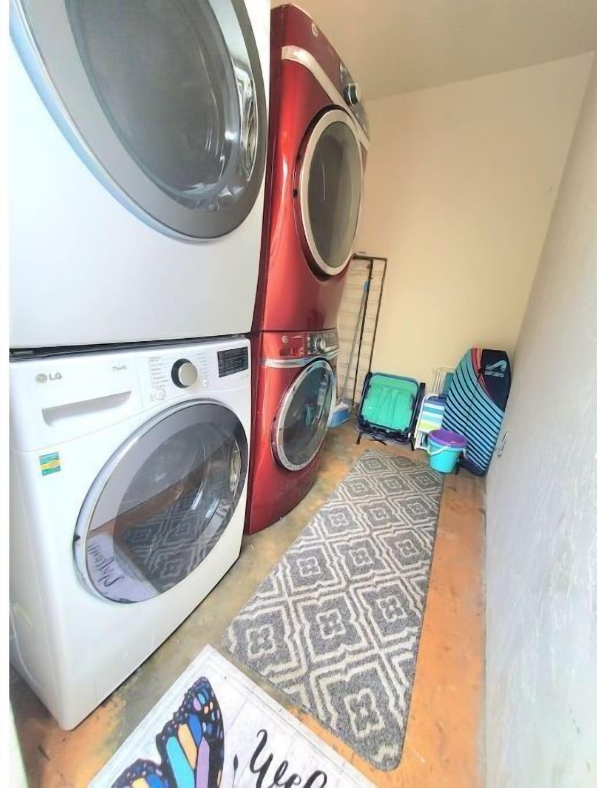 Un área de lavandería con dos lavadoras apiladas, un tapete estampado y una mesa plegable verde.