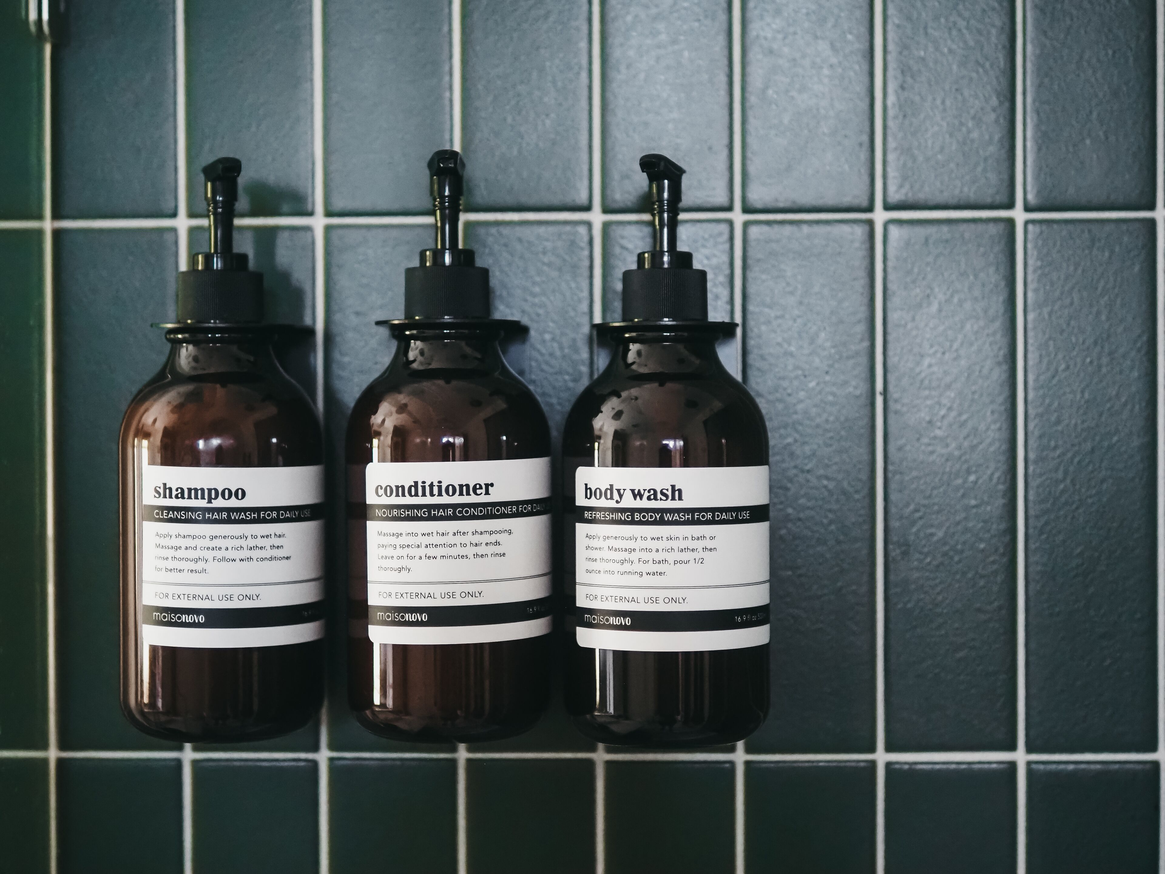 Three bottles of hair care products against a tiled wall.