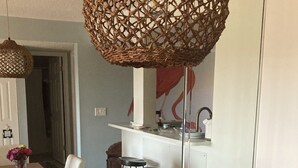 Zona de dinar moderna amb taula de fusta, cadires blanques i llum penjant de fibra.