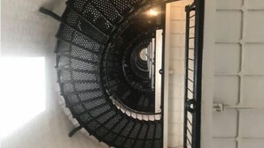 Una escala de caragol amb barana de metall negre i paret blanca.