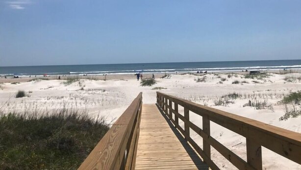 Un camí de fusta que condueix a una platja amb dunes i l'oceà al fons.