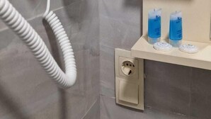 A bathroom with a hairdryer on a wall-mounted stand, a towel rack, and two bottles of blue liquid on a shelf. - Salami Residence (Batumi)