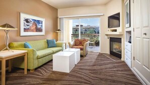 A hotel room with a green sofa, white coffee table, and a fireplace. There is a balcony with a view of buildings and a mountain. - 1BD Las Vegas Boulevard w/Lazy river, Shuttle and near the Strip! (Las Vegas)