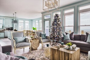 A spacious living area with a large window, a Christmas tree, and a cozy seating arrangement. - Oceanview Holiday! Hot Tub + Pool (Topsail Beach)
