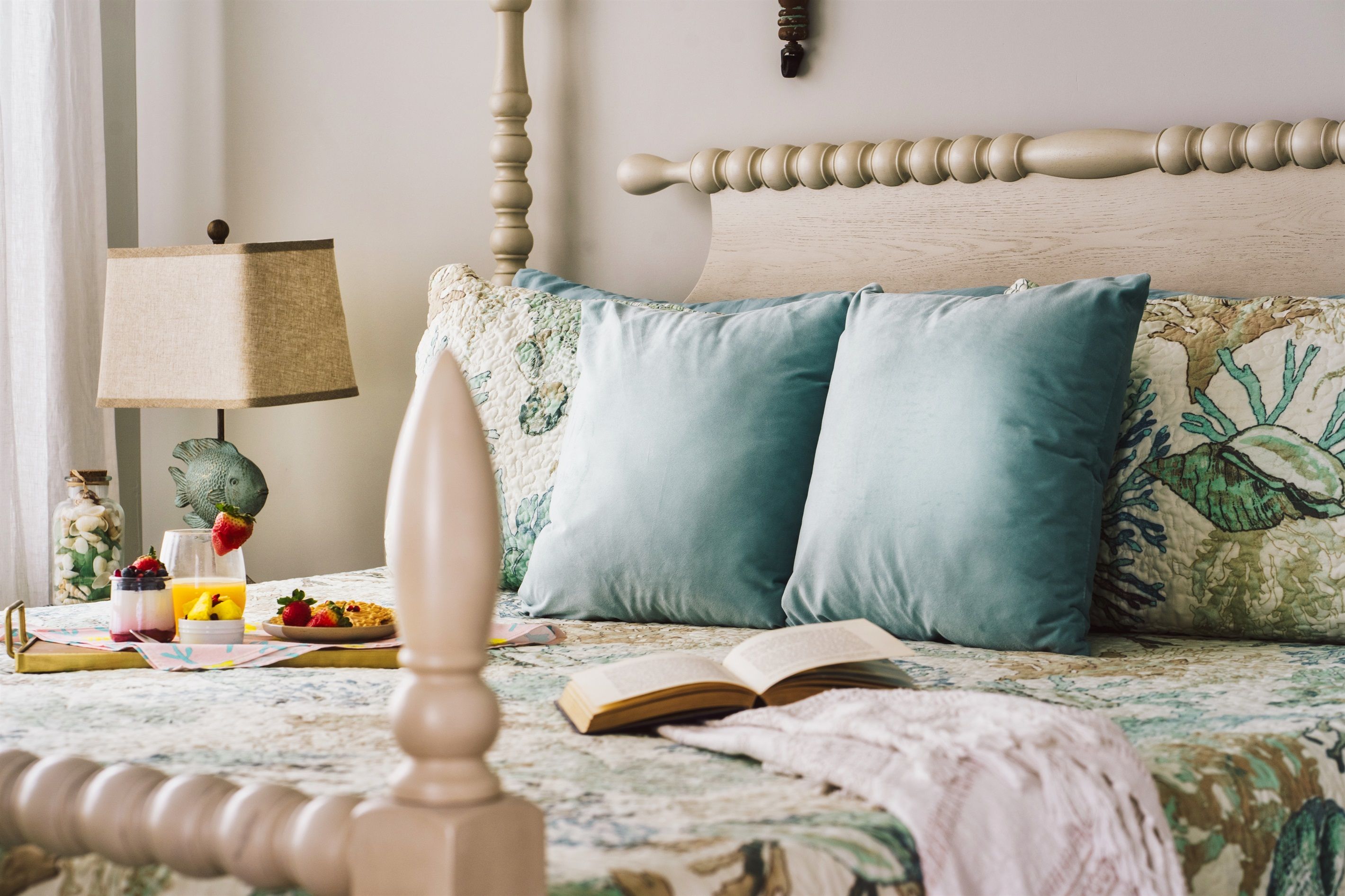 A bedroom with a bed, a bedside table with a lamp, a book, and a decorative plant.