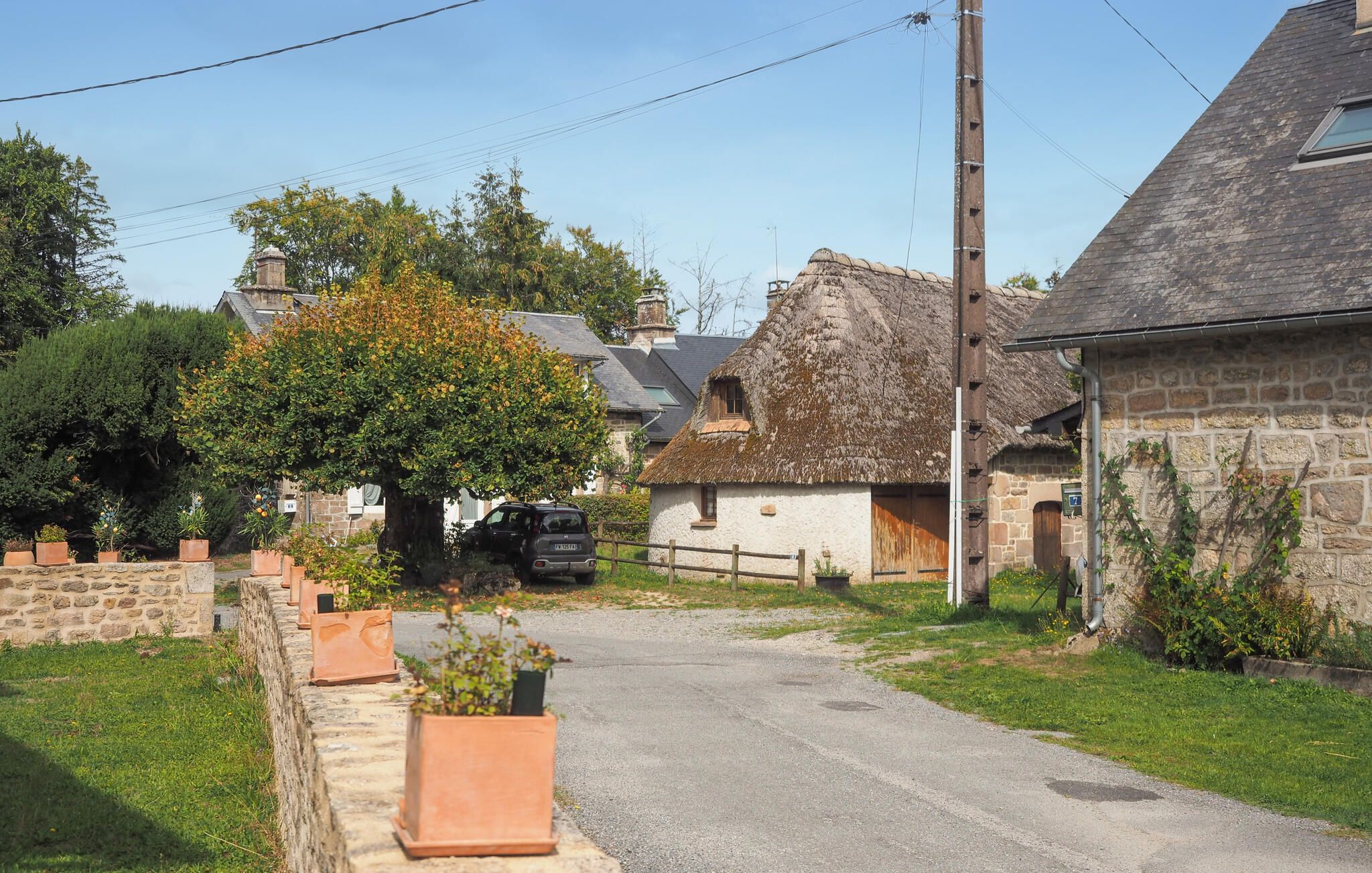 Una calle rural con muros de piedra, una casa con techo de paja y un coche estacionado.