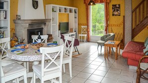Un coin repas avec une cheminée, des chaises blanches, une table avec des assiettes et des œufs, et un téléviseur en arrière-plan.